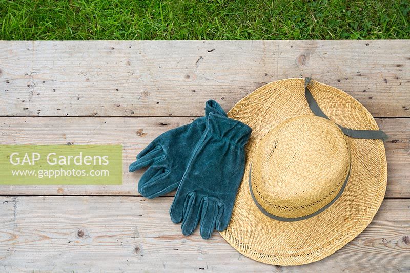 Summer hat and suede gardening gloves on wooden surface