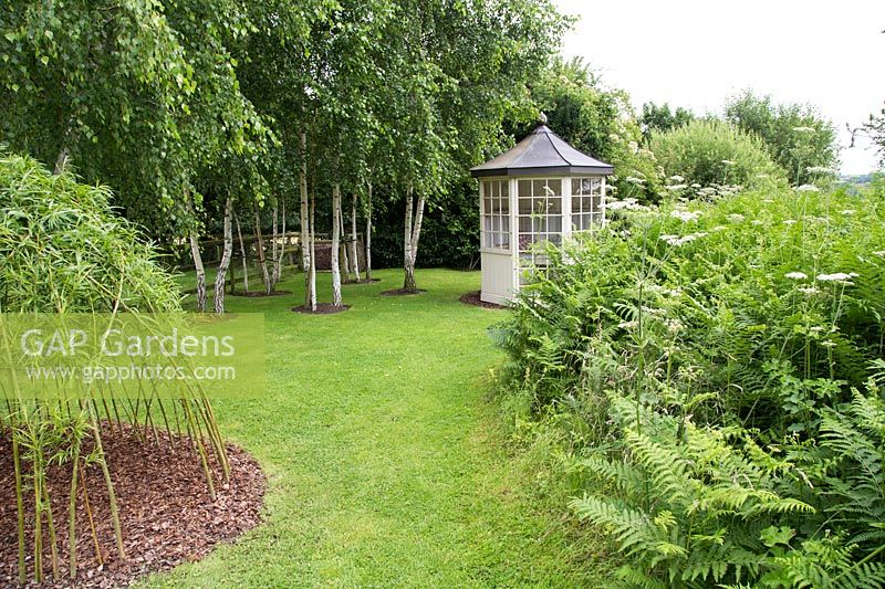 A woven Willow structure with Birch trees and summerhouse in background