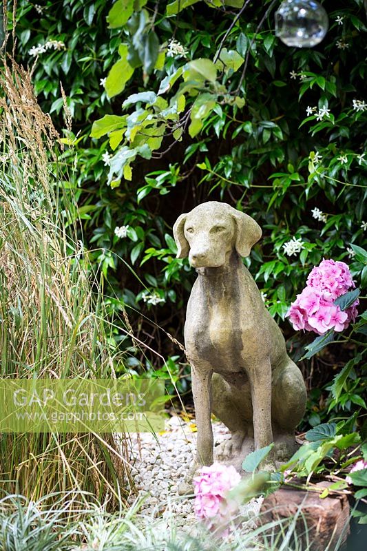Small garden with dog statue in gravel with grasses. Hackney, London