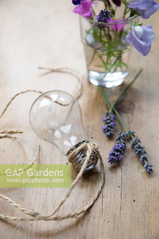 Making hanging flower vases from lightbulbs. Once all the inside of the bulb have been removed fasten the string or wire tightly around the ribbed metal section of the bulb, for hanging.
