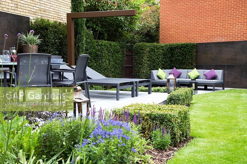 Contemporary suburban garden with copper feature wall, patio with dining furniture and hedging