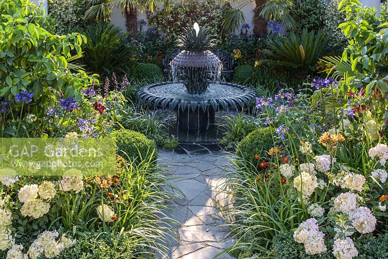 Crazy paving path leading to decorative water fountain with jasmine, salvias, agapanthus, lemons and cycads, box, ivies and hydrangeas - Great Gardens of the USA The Charleston Garden, RHS Hampton Court Palace Flower Show 2017 - Designer: Sadie May Stowell