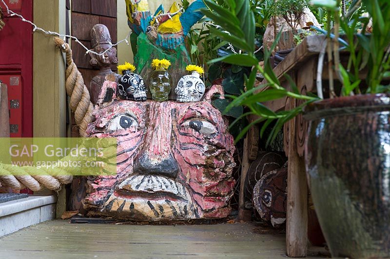 Carved and painted wooden tiger head outside the front door, with skull vases perched on top. Ginger plant - Hedychium sp. in the foreground. Sculptor and ceramicist Marcia Donahue's garden in Berkeley, California.