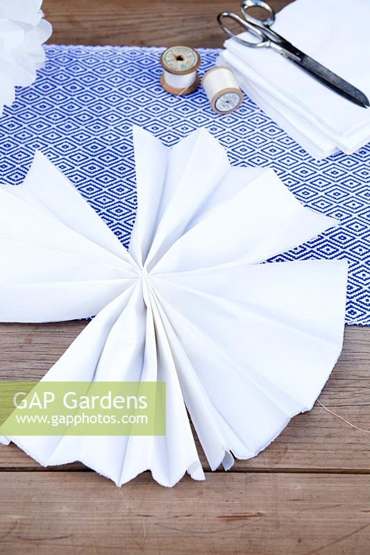 Making a paper pom pom from napkins. The 2 fastened strips of folded napkins should fold up in to a fan shape