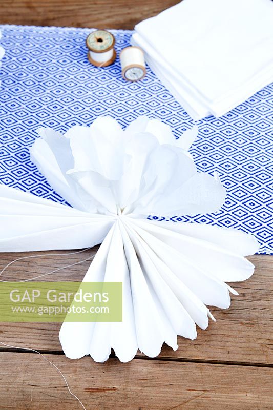 Making a paper pom pom from napkins. Separate the layers of paper fan and start to pull them upwards to form a pompom ball.