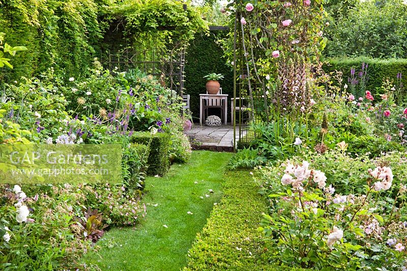 Grass path between borders of perennials and Roses leading to patio - Hetty van Baalen garden, Netherlands