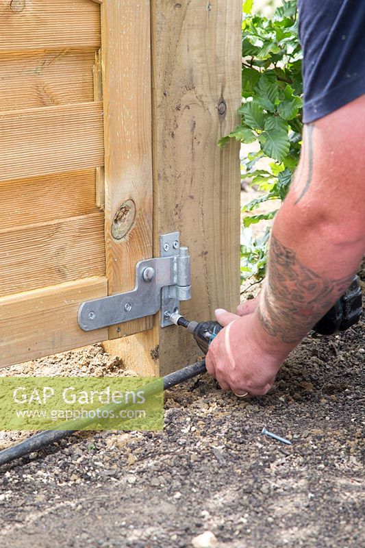Man fixing gate to post with elcetric screwdriver