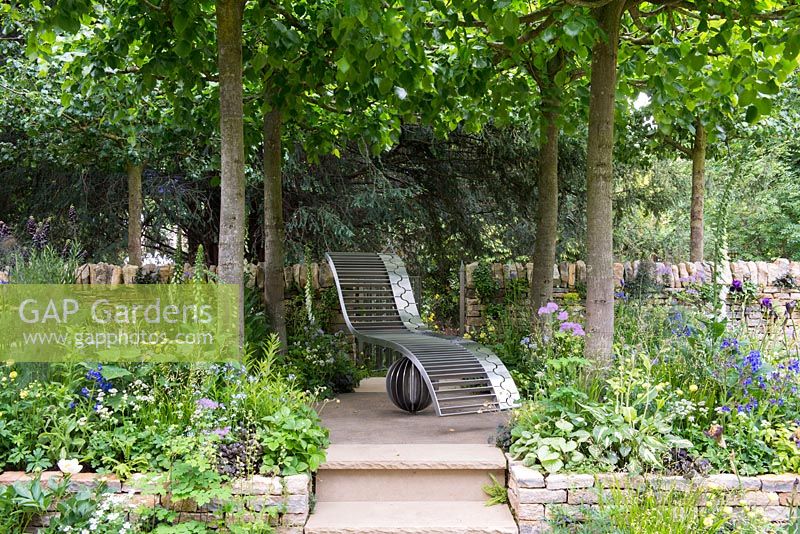 The Poetry Lover's Garden - Steel chaise longue under Lime trees, Tilia x europaea -  RHS Chelsea Flower Show 2017