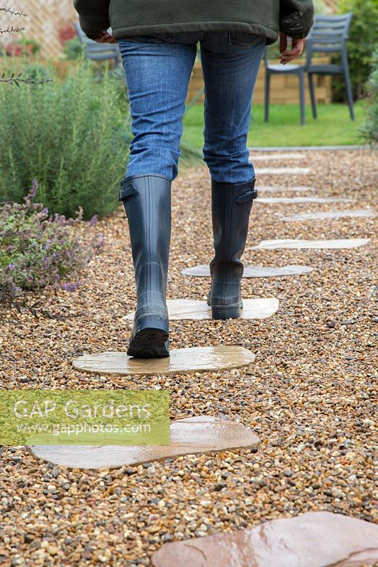 Woman in wellington boots walking on stepping stones through gravel garden