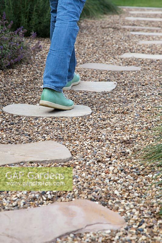 Woman walking on stepping stones through gravel garden
