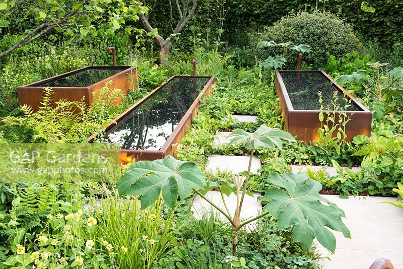 Rusted water troughs set in lush green planting - BBC Radio 2 Feel Good Gardens - The Zoe Ball Listening Garden, RHS Chelsea Flower Show 2017 - Designer:  James Alexander-Sinclair