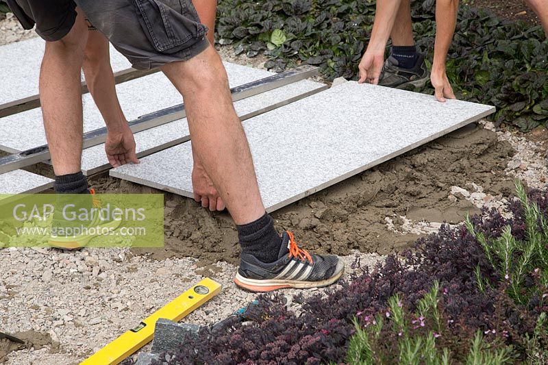 Making a mixed material patio - two men placing large porcelain slab on mortar bed