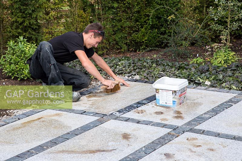 Making a mixed material patio - man using jointing compound on patio with mix of large porcelain slabs and granite setts