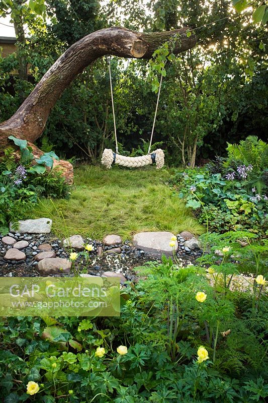 Tree rope swing in wild garden next to the  stream with stones. The Zoflora and Caudwell Children's Wild Garden - RHS Hampton Court Palace Flower Show 2017