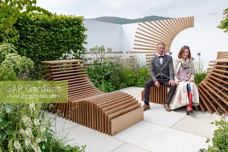 Designers, Denis Kalashnikov and Ekaterina Bolotova, sitting on slatted reclining spa chairs surrounded by soft planting of Alliums and Angelica archangelica - Spa Garden - Molecular Garden, RHS Malvern Spring Festival 2017 