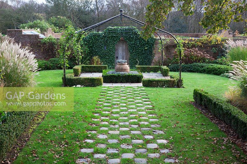 Grass and stone setts form a chequered path to pergola covered small Buxus - box edged, Lavender filled  knot garden with terracotta urn - Brightling Down Farm