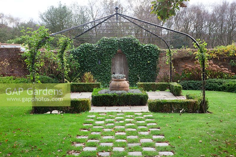 Grass and stone setts form a chequered path to pergola covered small Buxus - box edged, Lavender filled knot garden with terracotta urn - Brightling Down Farm
