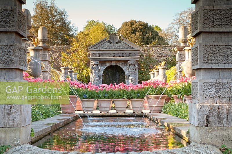 Tulipa 'Pink Impression' in containers alongside pool and Italianate water fountains in The Collector Earl's Garden at Arundel Castle, Sussex in spring. Head Gardener: Martin Duncan