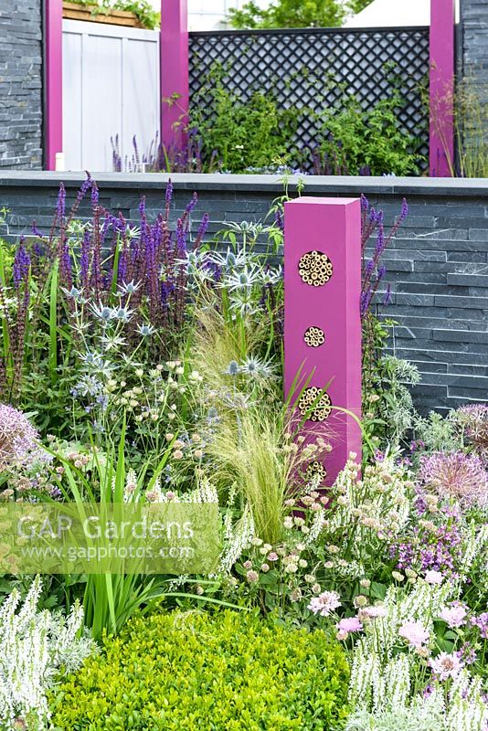 Bug hotel and planting in pink, blue and white with Salvia, Stipa and Allium  in outdoor kitchen with bug hotels, grey stone wall  - BBC Gardener's World Live, Birmingham 2017 - The Lanwarne Landscapes 'Contemporary Bee and Butterfly' Garden - Head Sponsors: IntoUniversity, Big City Bright Future Programme, Black Rock - Best Landscape Construction. Best Construction Landscaper