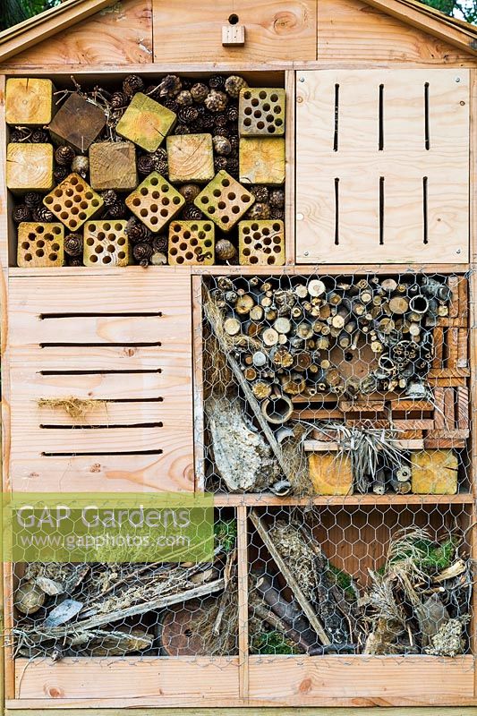 Insect hotel made of cut lumber, plywood, chicken wire, tree branches, bark and grass plants in summer