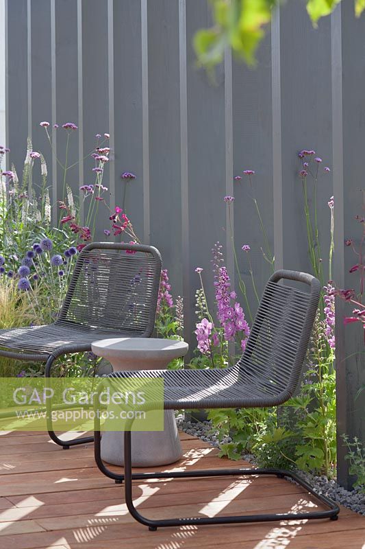 Chairs on all-weather mandioqueira wood decking with grey painted wooden vertical fence boards in the 'Business and Pleasure' Garden at Tatton RHS Flower Show 2017