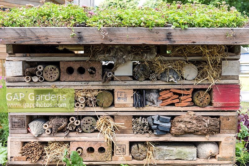 A bug hotel built from wood offcuts, leftover bricks, bamboo lengths, branches, straw and pipes.