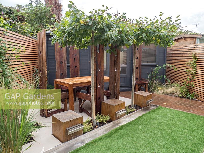 Contemporary small London garden with water feature, dining and entertaining area and office all brought together under the table top pleached trees