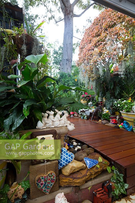 View from the covered entertaining area to a raised garden with timber decking. Eclectic collection of pots and garden ornaments featuring ceramic hearts and a rabbit ornament.