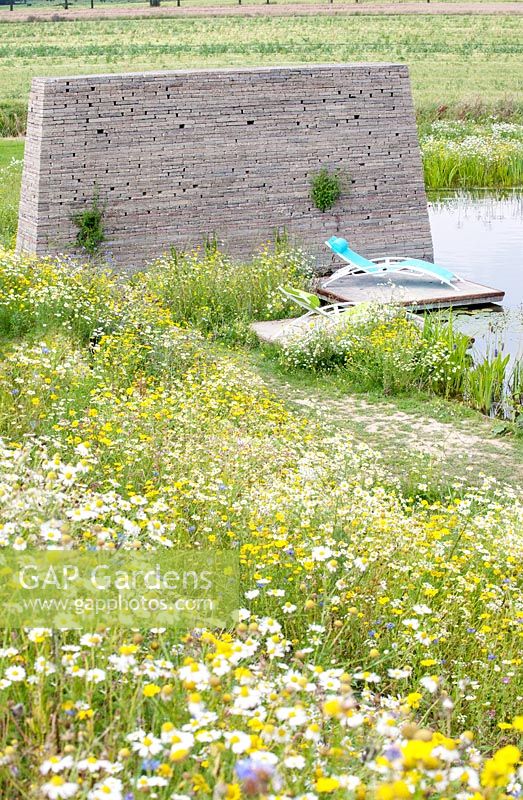 Surrounded with wildflowers swimming pond with tower made of recycled paving tiles near a concrete jetty.