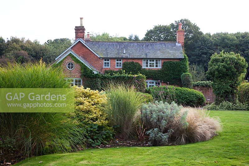 View of the house with island beds planted with shrubs and grasses including, Miscanthus, Euonymus and Stipa tenuissima.