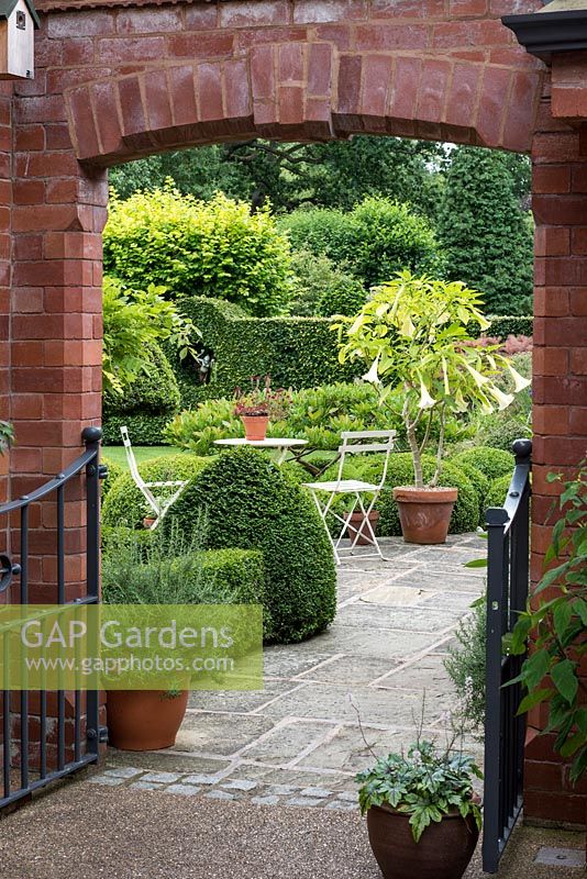 Framed by gateway in a brick wall, the view of a half-acre town garden with topiary, terrace and lawn.