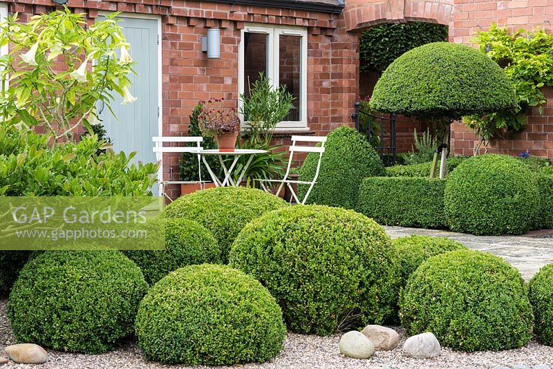 Seating area in the corner of a stone terrace, punctuated by box topiary.