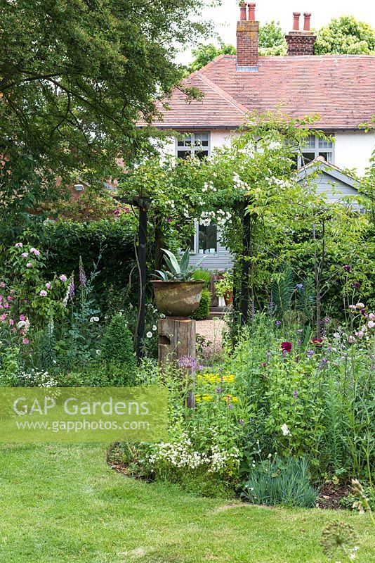 In a long town garden, a rose arch leads from a middle area of flower borders, to a gravel courtyard beside the house.