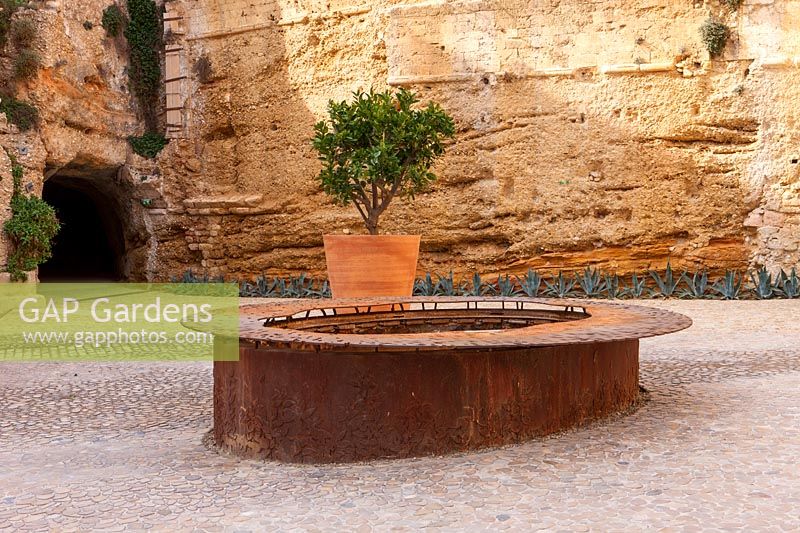 Rusty metal pool with orange tree in planter, Jardin de Migrations, Saint Jean, Marseilles, France, February.