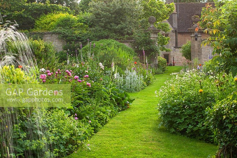Perennial borders and fountain spra with grass path at Pytts place, Burford, June.