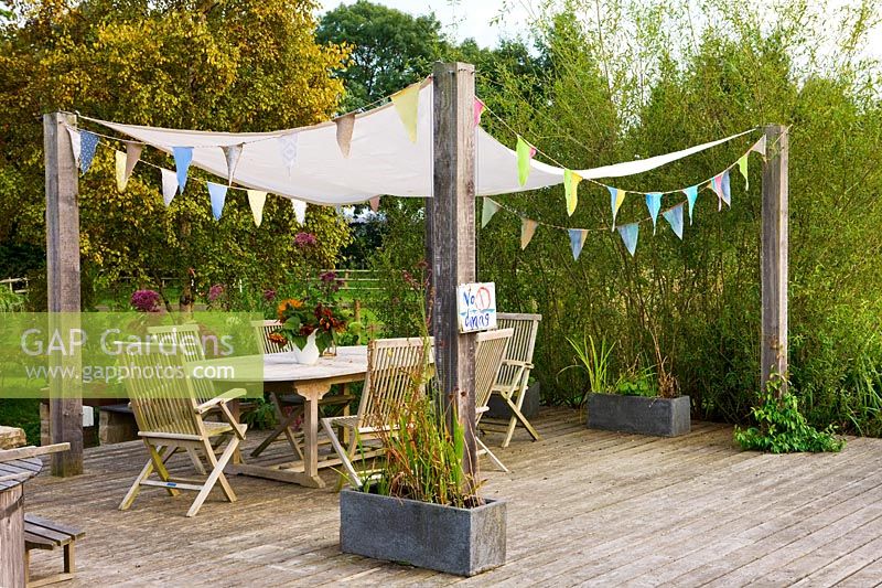 Wooden decking seating area with pergola fitted with shade sail and bunting
