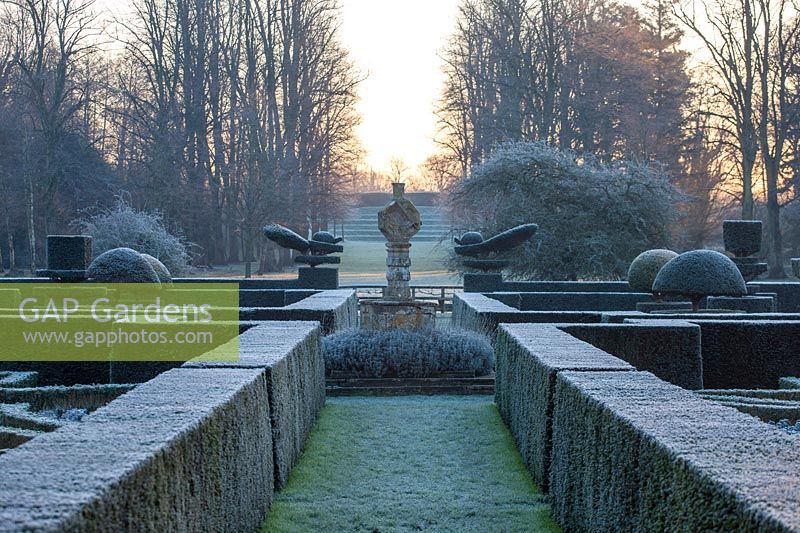 Winter view along axis of parterre garden with formal clipped yew hedging and topiary shapes to stone focal point
