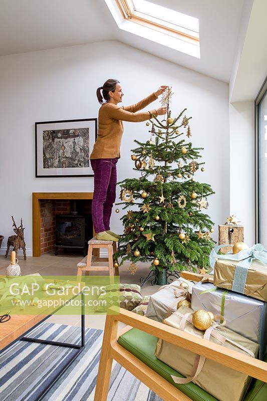 Woman decorating gold colour themed Christmas tree in living room