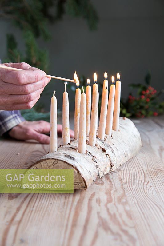 Close up detail of lighting beeswax candles in Birch wood candle holder