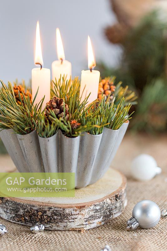 Festive candle holder made from cooking mould filled with pine foliage and cones in festive table setting with decorations