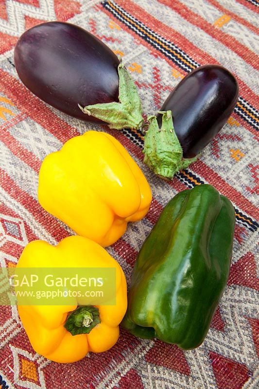 Colourful fresh vegetables - Yellow and green peppers with aubergines on a kilim covered table