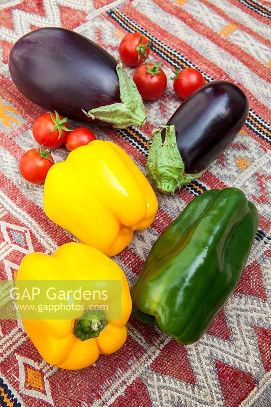 Colourful fresh vegetables - Yellow and green peppers with aubergines and cherry tomatoes on a kilim covered table