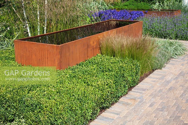 Contemporary garden with rusted corten steel water trough and green foliage planting. RHS Hampton Court Flower Show