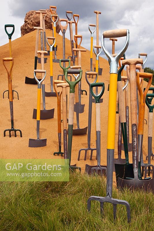 Conceptual garden with garden tools in sand at RHS Hampton Court Flower Show