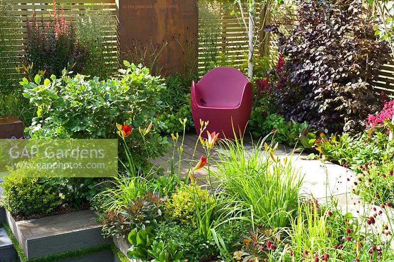 Contemporary garden with slatted fence, pink seat and a bright planting combination with foliage plants and perennials