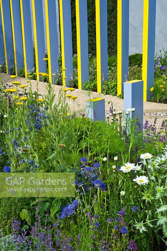 Garden feature of painted upright pergola columns lining a gravel path. RHS Hampton Court Palace Flower Show