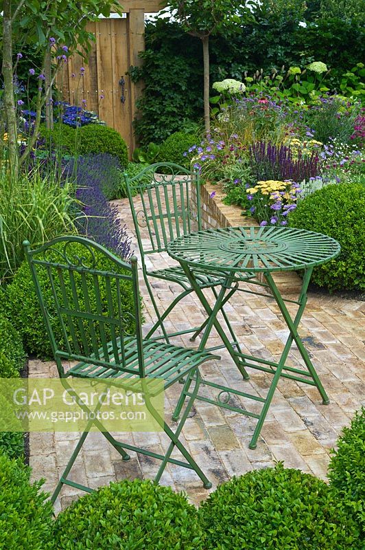 Small wirework table and chairs in a brick paving area of a garden