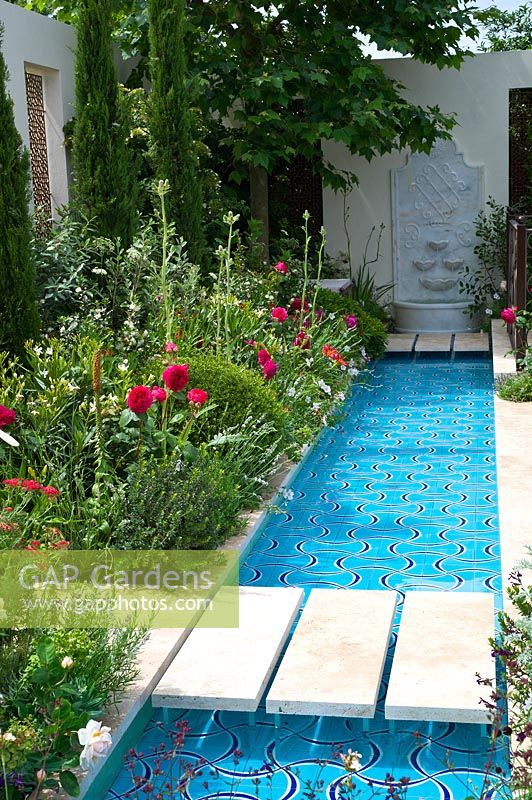 A wide rill of water with lush borders beside a seating area in the Turkish Ministry of Culture and Tourism: Garden of Paradise.