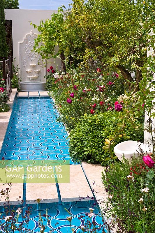 An exotic garden with a wide rill of water and lush borders of Pomegranate trees and roses
