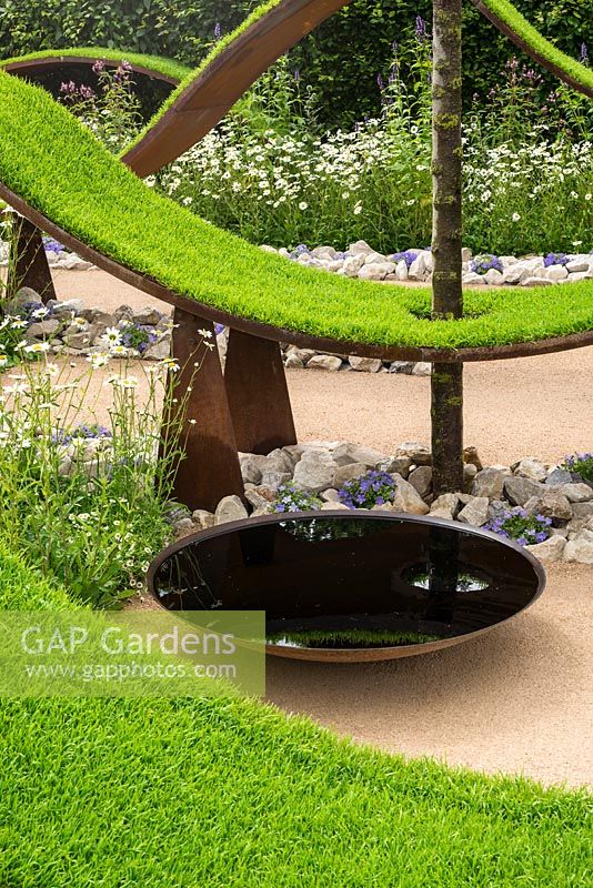 Undulating waves of artificial turf, with circular bowl water feature. RHS Hampton Court flower Show